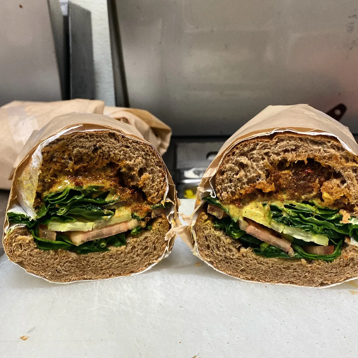 Don's Delhi sandwich — falafel with sun-dried tomato and curry mayo, spinach, cucumbers, tomato and red onions, sliced in half on a wheat roll